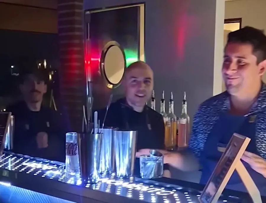 Bartenders sonriendo detrás de una barra iluminada durante una fiesta